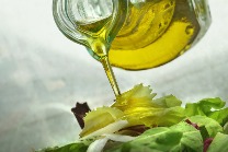 Olivenöl wird aus einer Karaffe auf Salat gegeben.